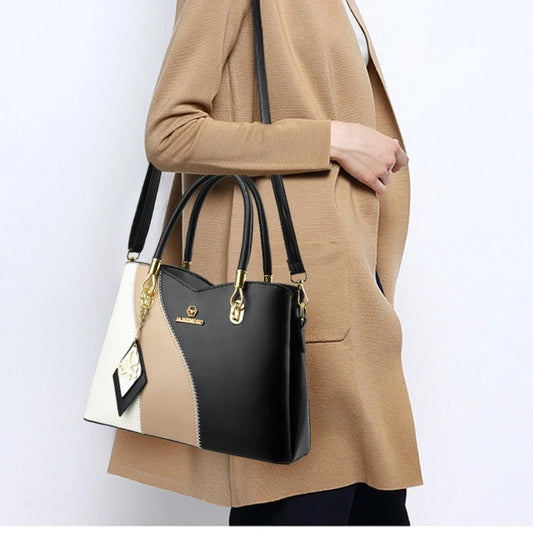 Woman wearing a tan coat carrying a tri-color black, beige, and white handbag.